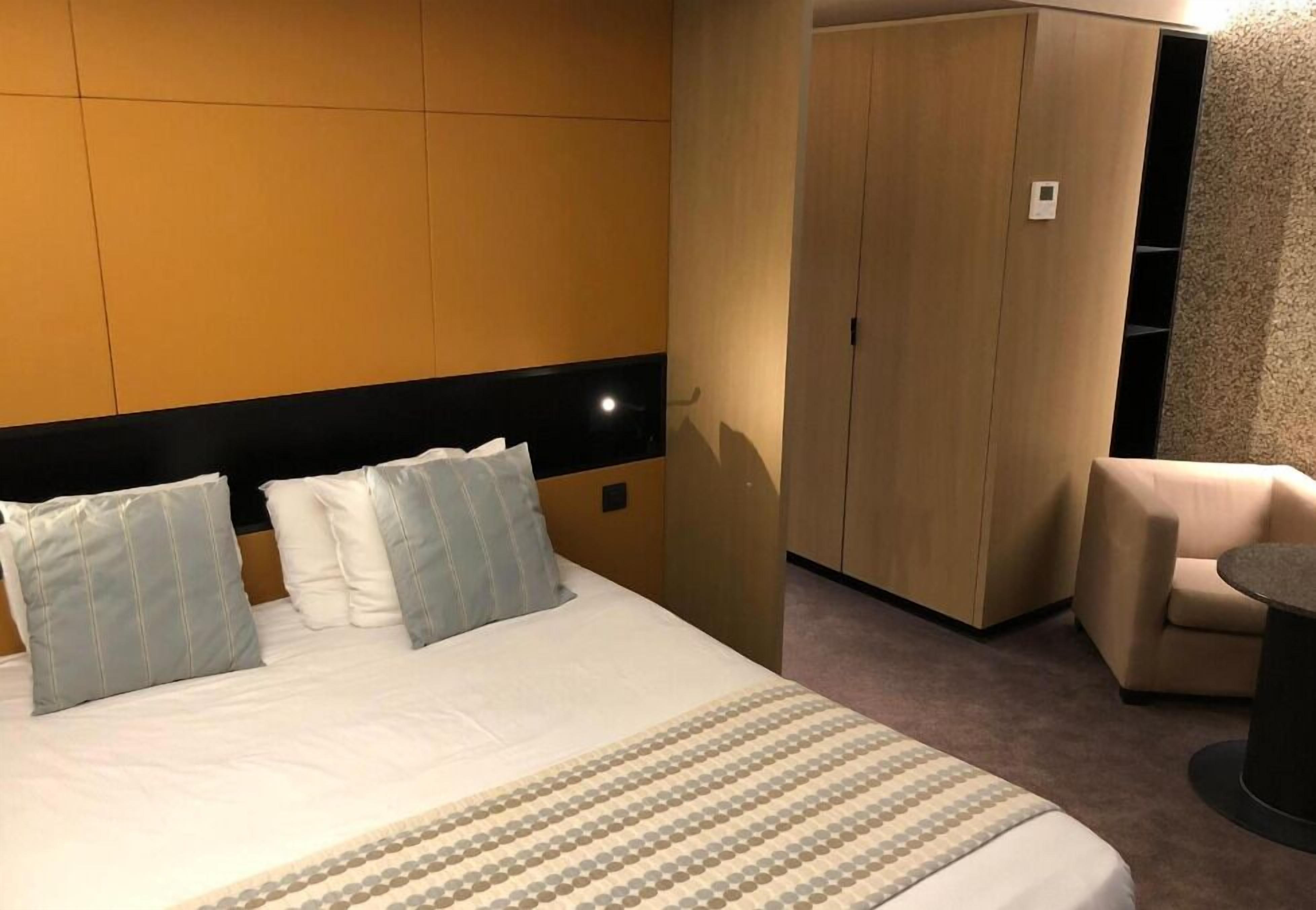 Una habitació d'hotel amb un llit, un armari, una zona de seients i una taula petita.