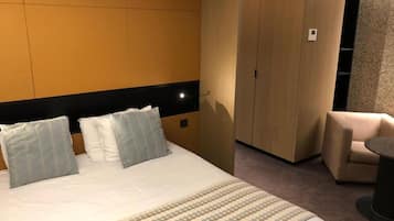 A hotel room with a bed, a wardrobe, a seating area, and a small table.
