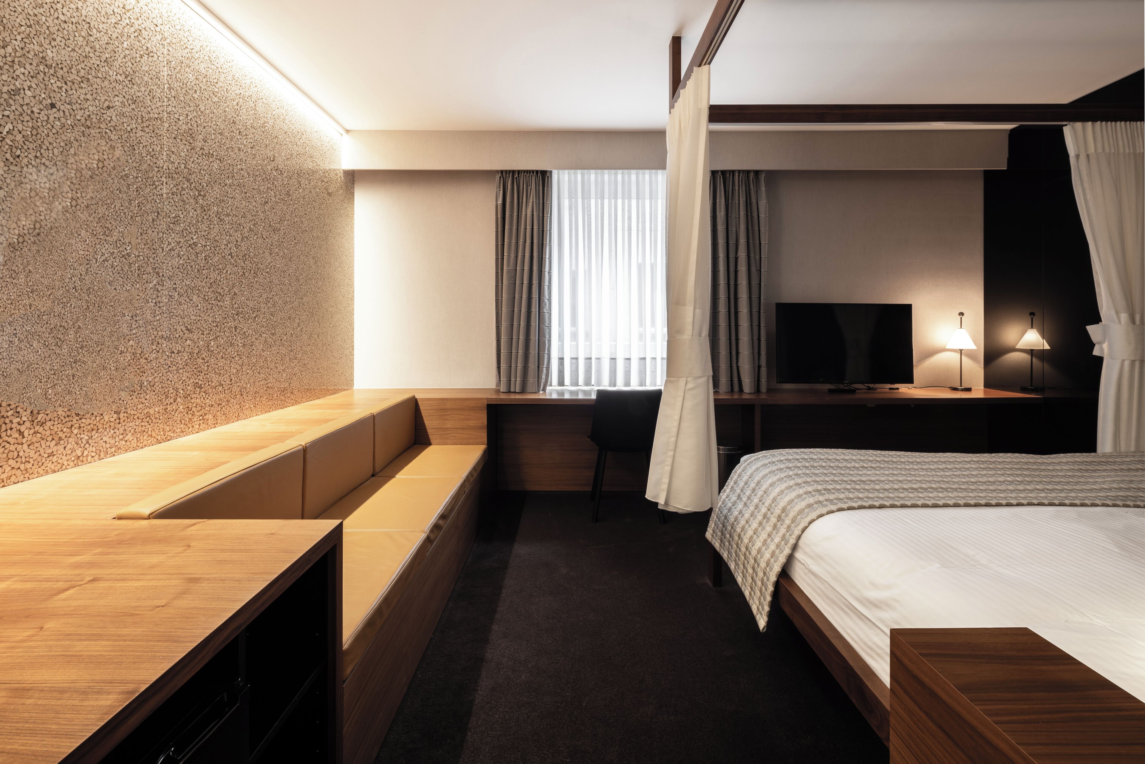 A modern hotel room with a wooden desk, a bed with a white comforter, a television, and a lamp.