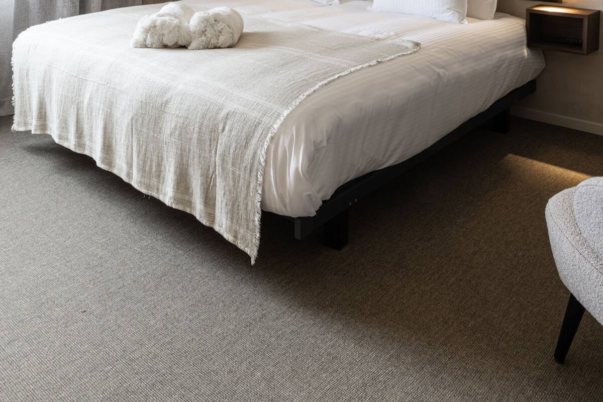 Una cama bien tendida con una colcha blanca y almohadas, dos lámparas de noche y una mesita de noche con lámpara.