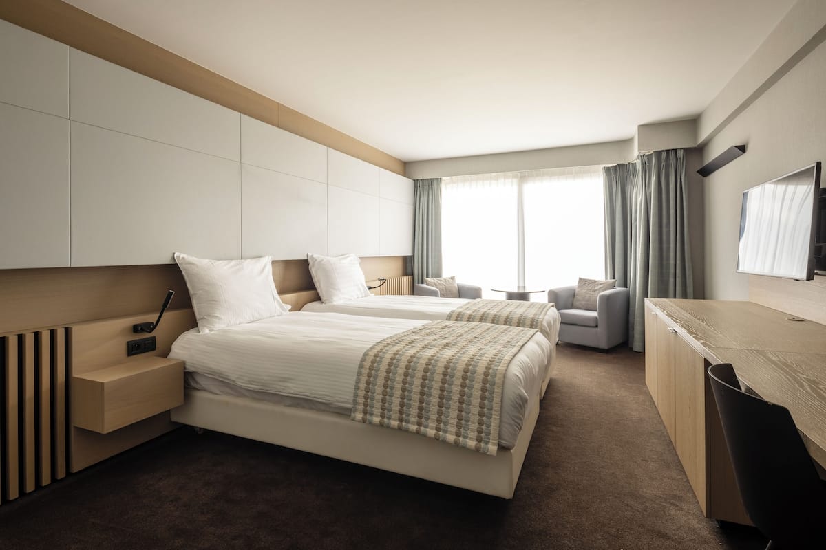 Una habitación de hotel moderna con dos camas, un escritorio, una silla y un televisor.