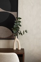 Un florero con una planta sobre una mesa de madera frente a una pared con arte abstracto.