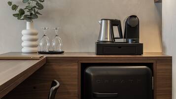 Una kitchenette compacta con cafetera, un refrigerador pequeño y un florero con una planta.