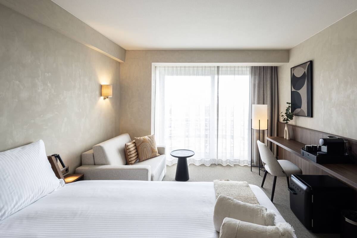 Habitación de hotel con una cama grande, un escritorio, una silla, una mesita y una ventana con cortinas.