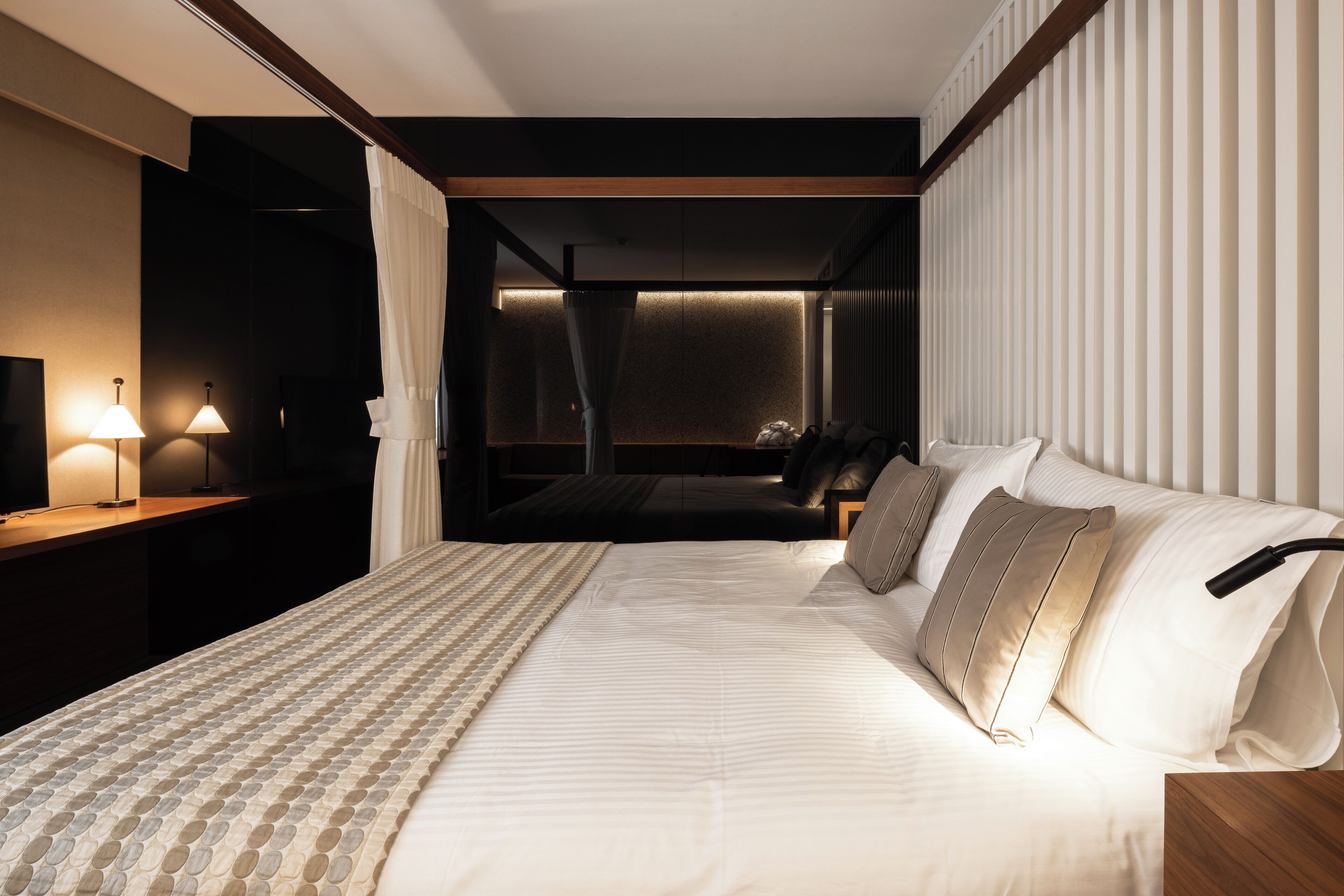 Una habitación de hotel moderna con una cama grande, un escritorio con lámpara y vistas a la ciudad desde la ventana.