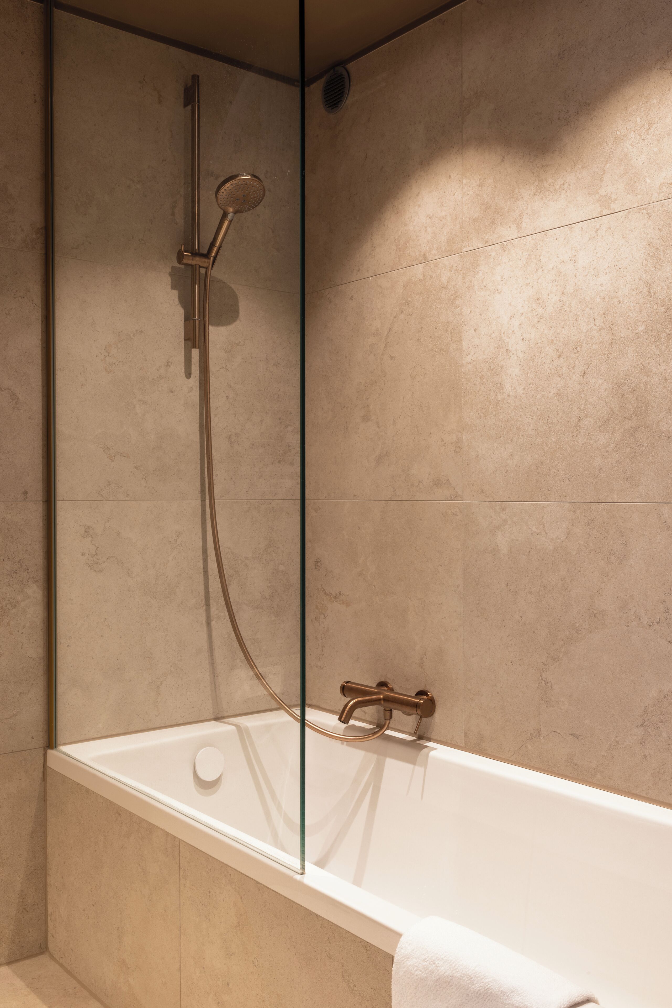 A modern bathroom with a glass-enclosed shower, a white bathtub, and a towel hanging on the side.