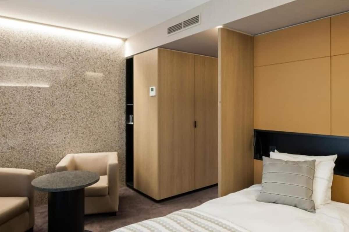 Una habitación de hotel moderna con una cama, una mesita redonda pequeña, un sofá y un armario.