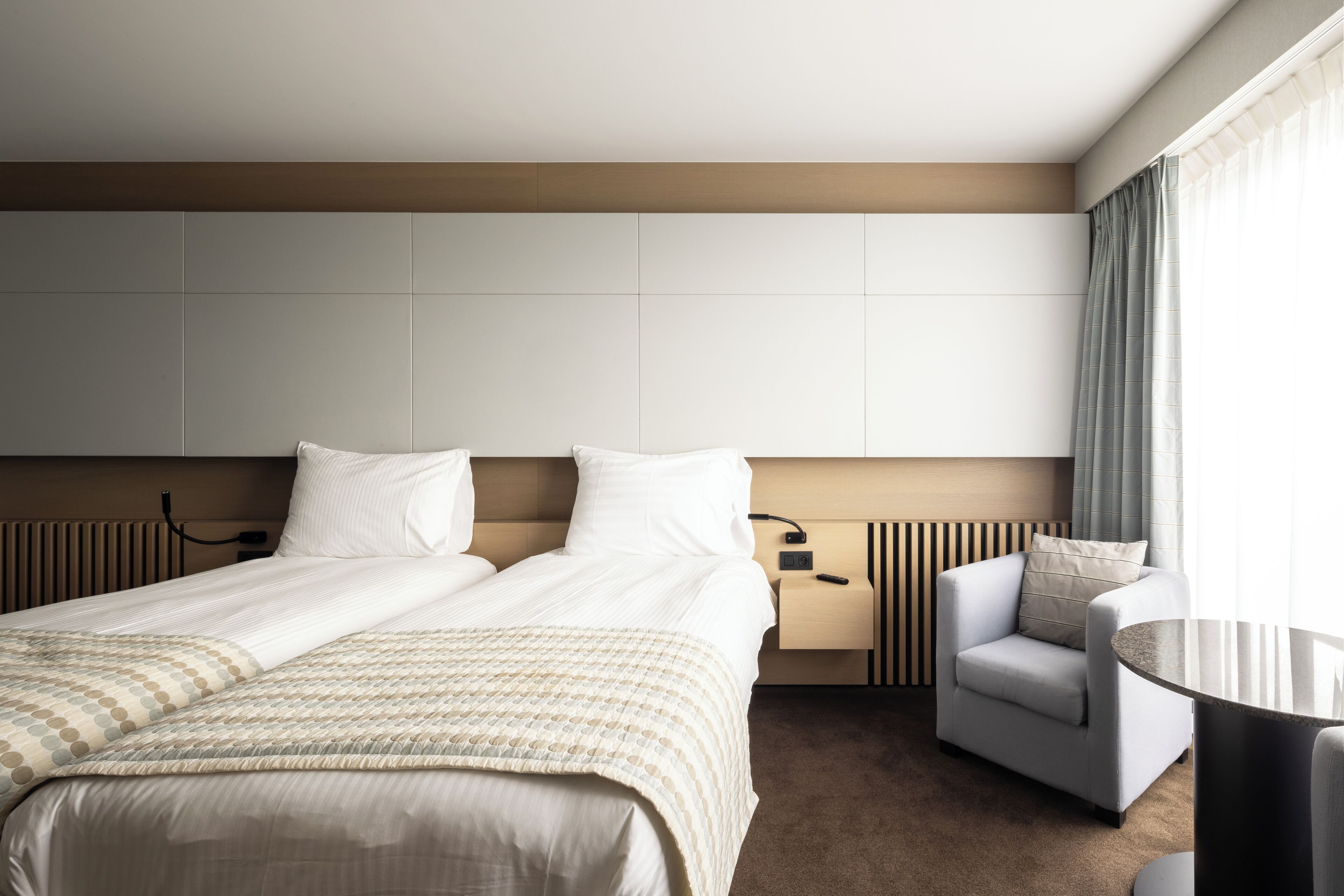 Ein Hotelzimmer mit einem großen Bett, einem Sessel, einem kleinen Tisch und einem Fenster mit Vorhängen.