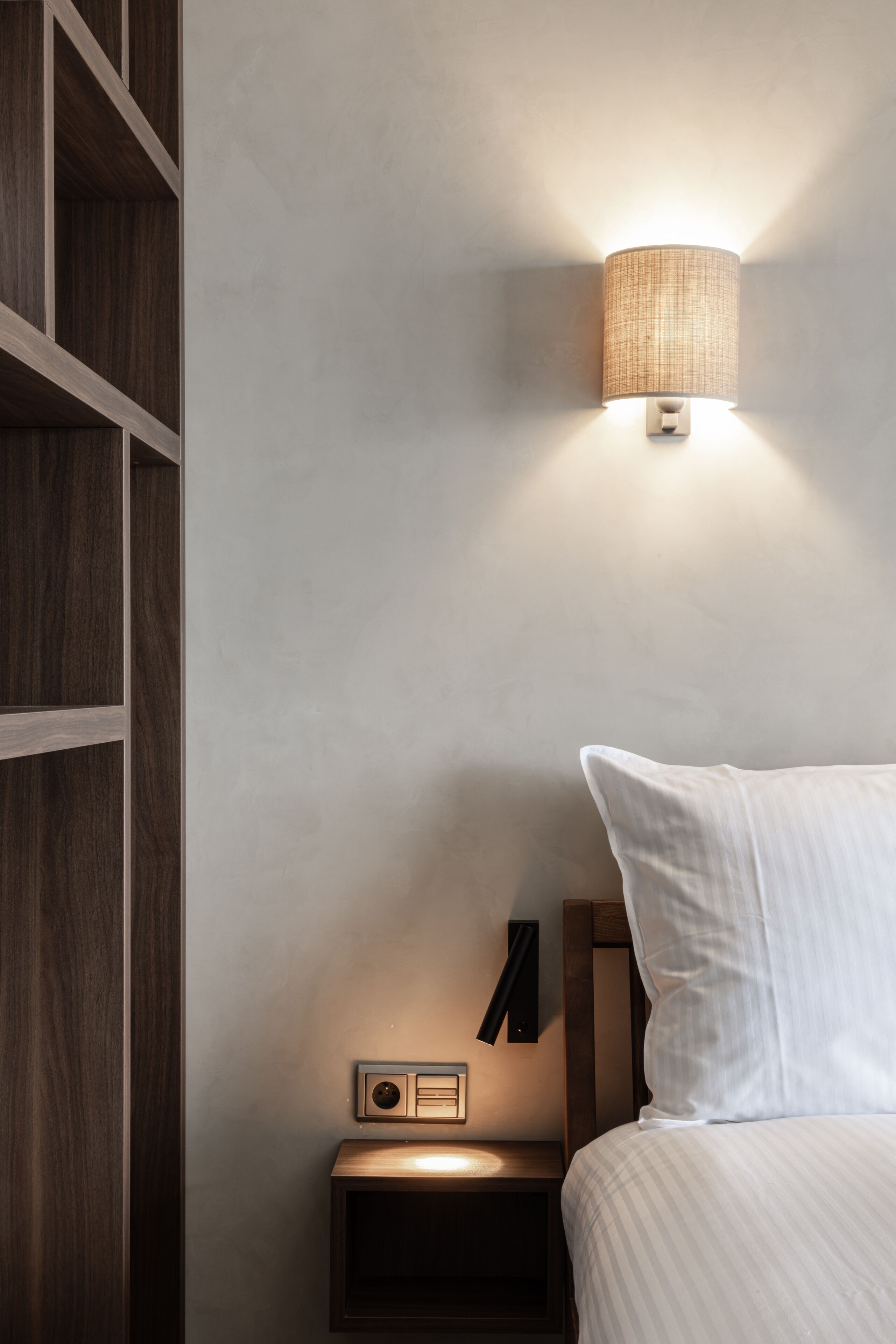 A bedroom with a wooden nightstand, a radio, and a wall-mounted lamp.