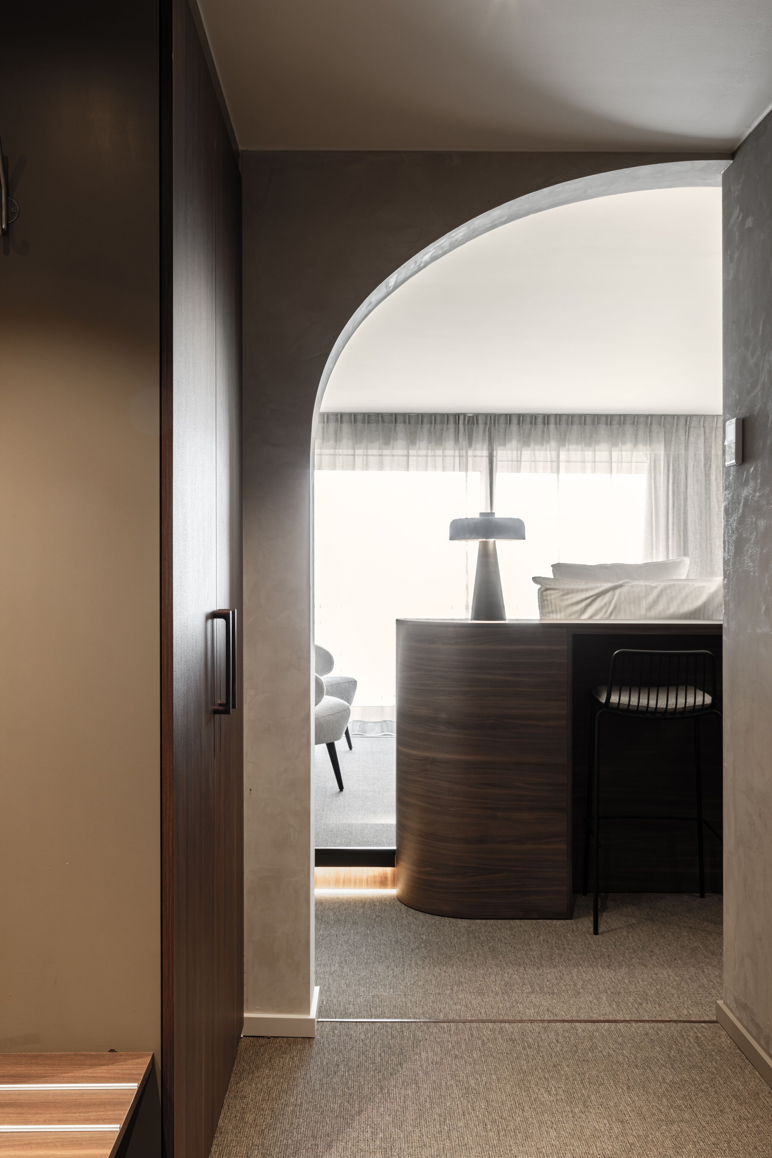 Una habitación de hotel moderna con techo curvo, una cama con mesita de noche, lámpara y vistas al exterior.