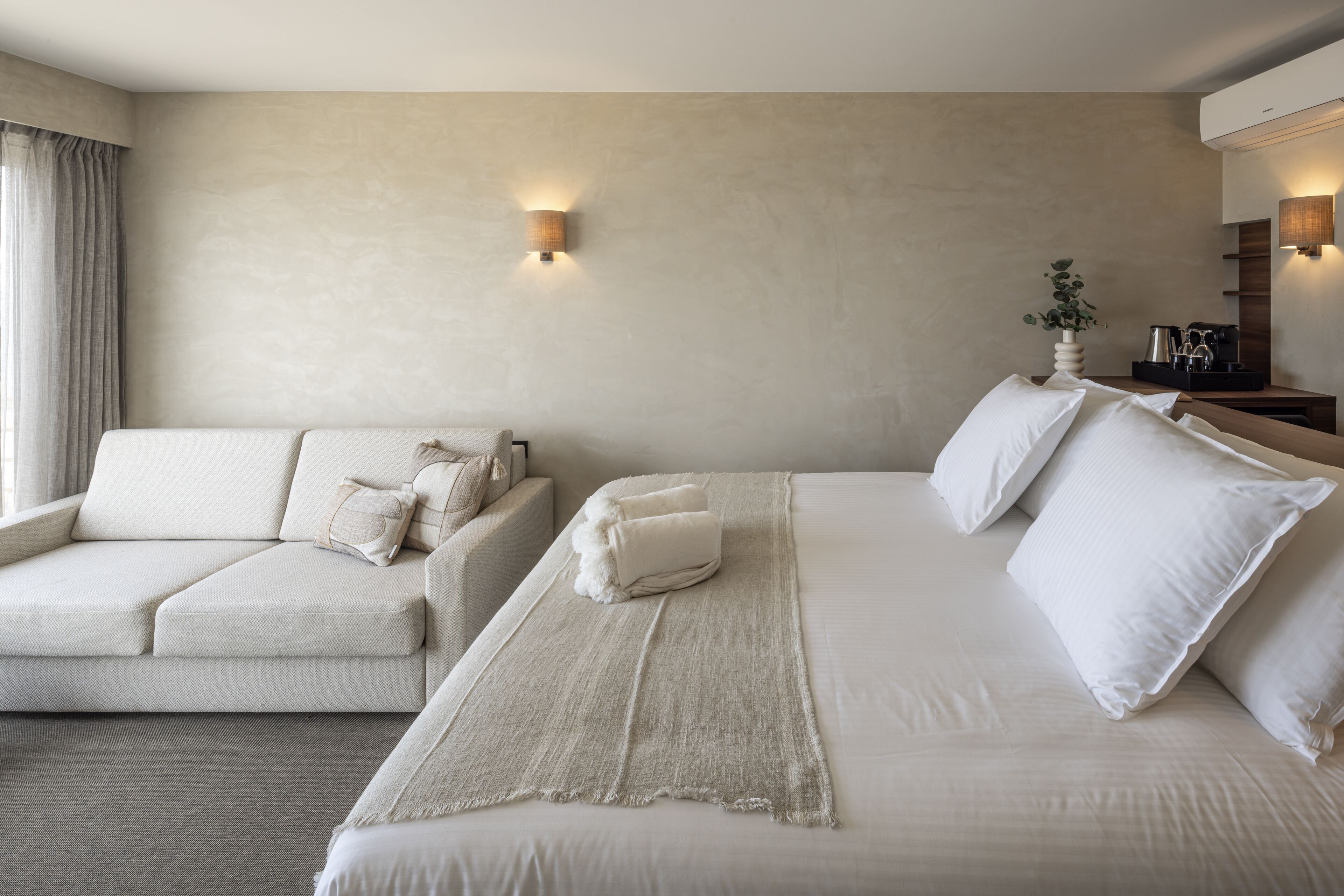 A hotel room with a large bed, a sofa, and a small table with a vase of flowers.