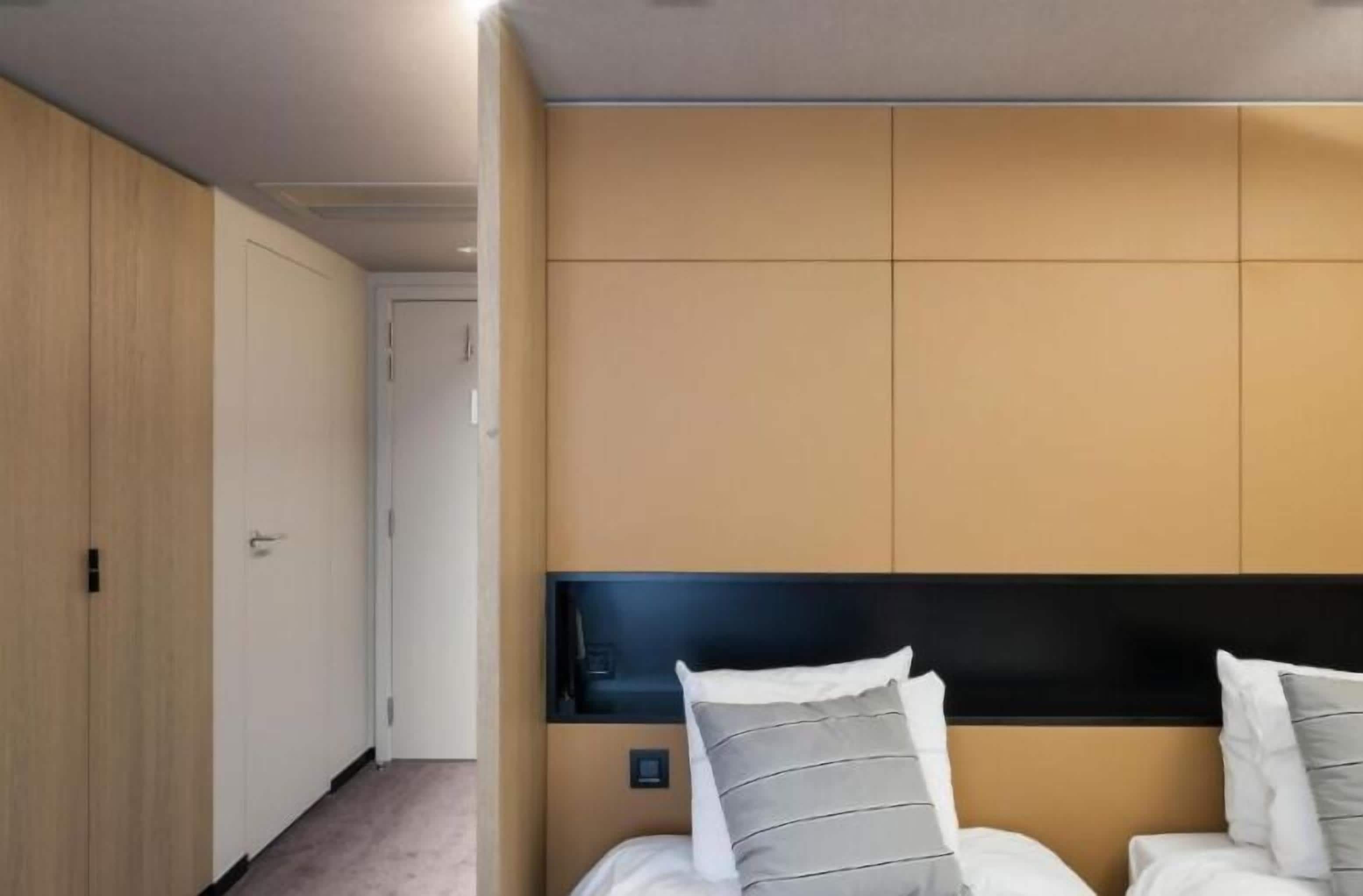 A hotel room with a bed, a headboard, a wardrobe, and a door.