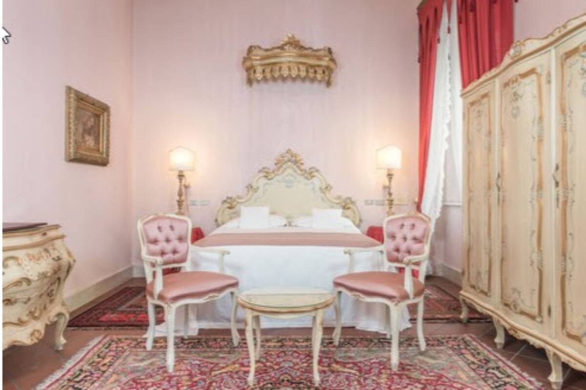 A bedroom with a large bed, two chairs, a small table, a wardrobe, and a patterned rug.