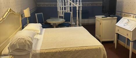 Un dormitorio con cama, mesita de noche, lámpara, escritorio, silla y televisor.