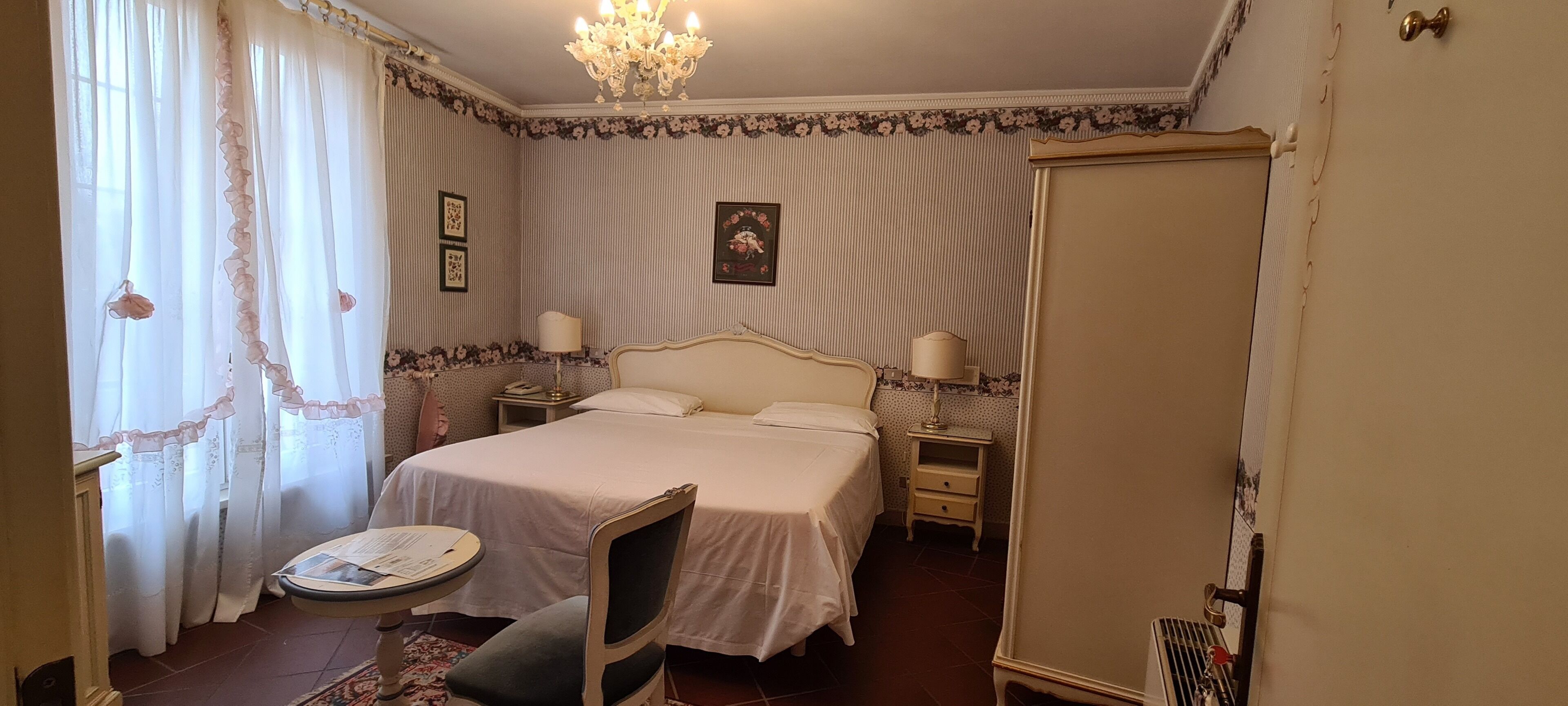 A bedroom with a large bed, bedside tables, a chair, a small table with a lamp, and a chandelier.