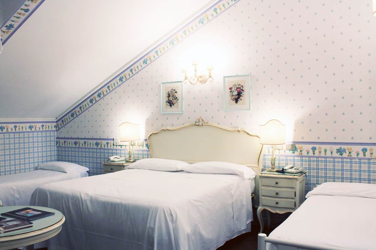 A hotel room with two beds, a round table, and a chandelier.