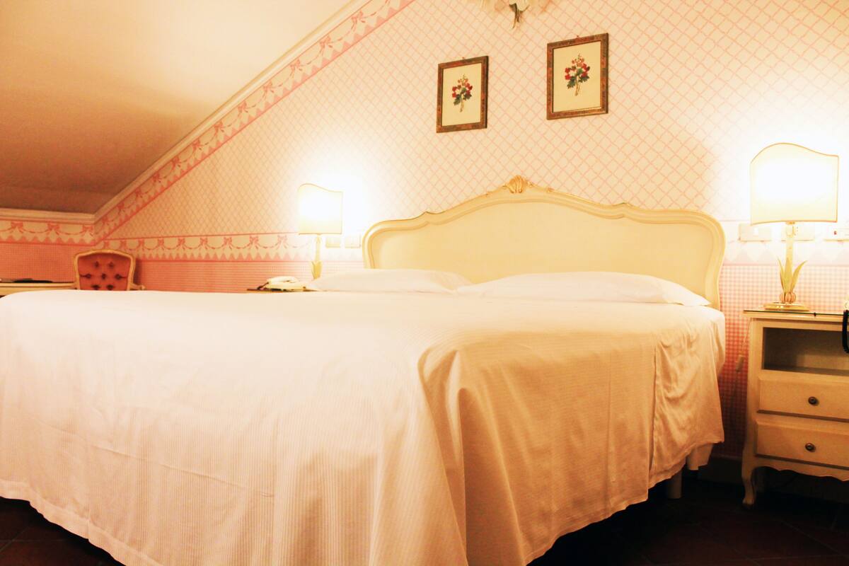 A hotel room with a large bed, two bedside lamps, a nightstand, and a chair.