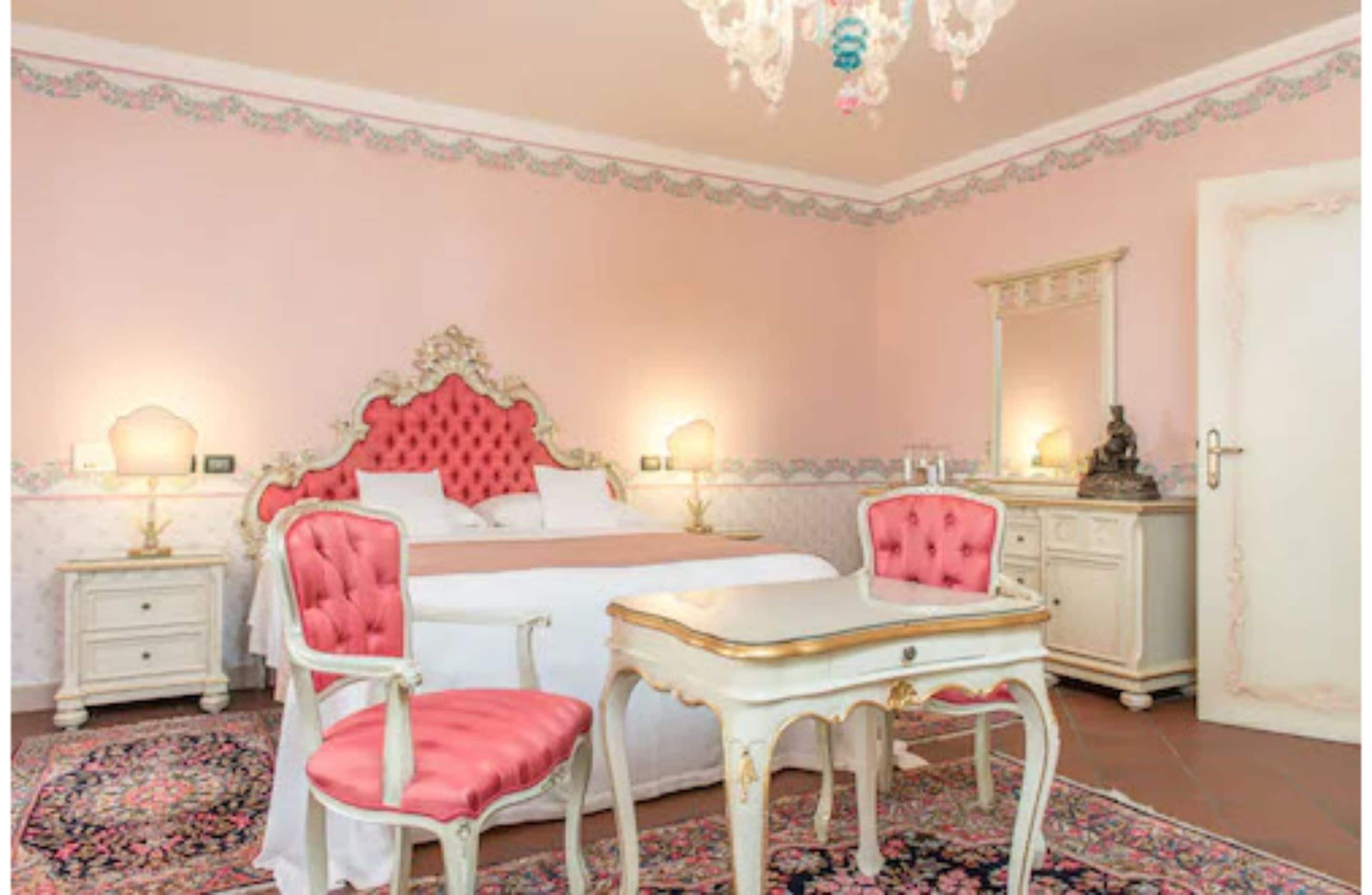 A bedroom with a large bed, two chairs, a dresser, and a mirror.
