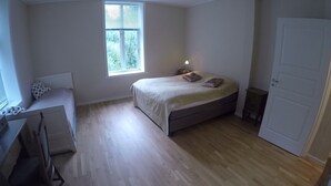 Un dormitorio con cama, escritorio, silla, ventana y puerta.