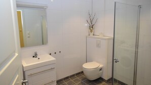 Un baño moderno con lavamanos blanco, inodoro y cabina de ducha de vidrio.