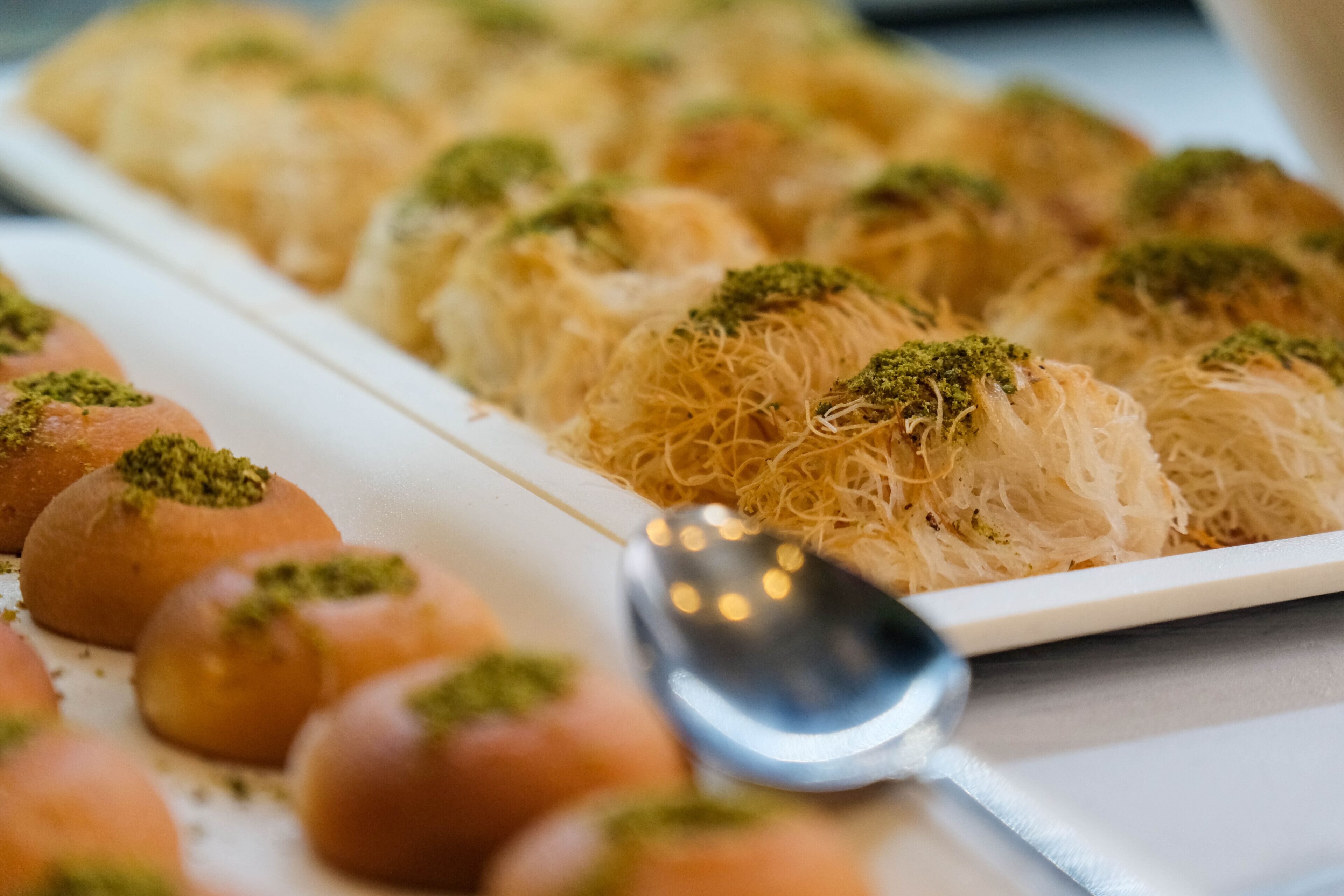 Un plato de baklava y pasteles redondos con una cuchara sobre la mesa.