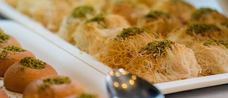 Un plato de baklava y pasteles redondos con una cuchara sobre la mesa.
