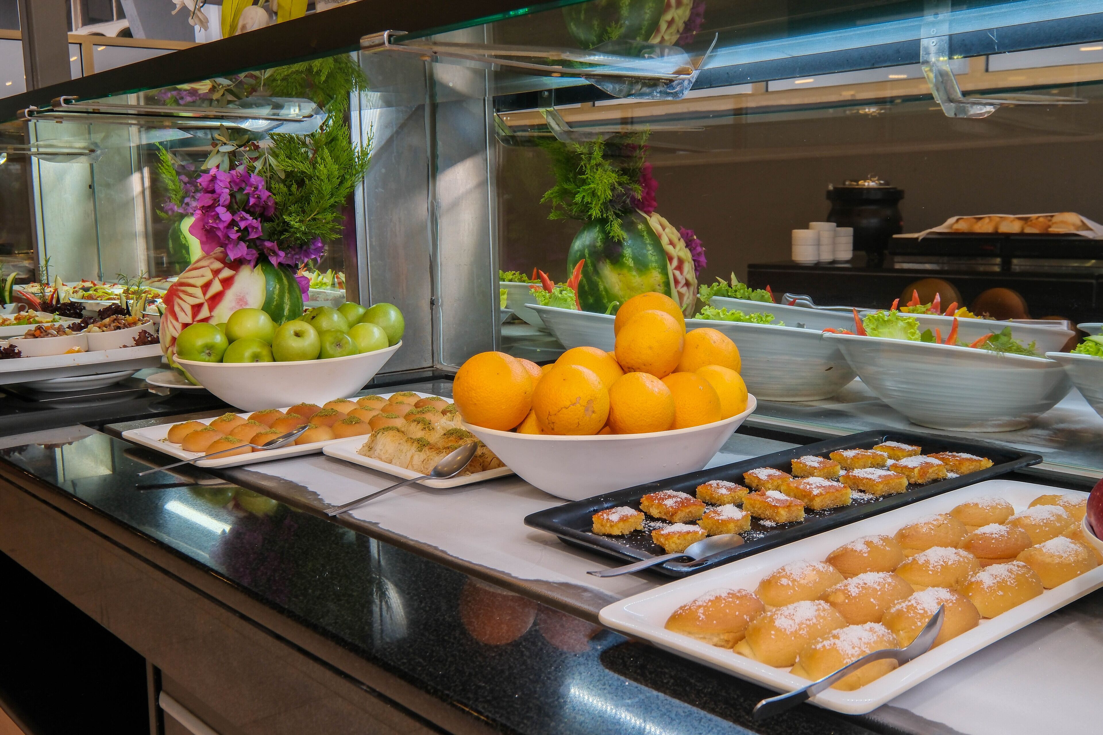 Un bufé con diversas opciones de comida, incluyendo frutas, verduras y postres.