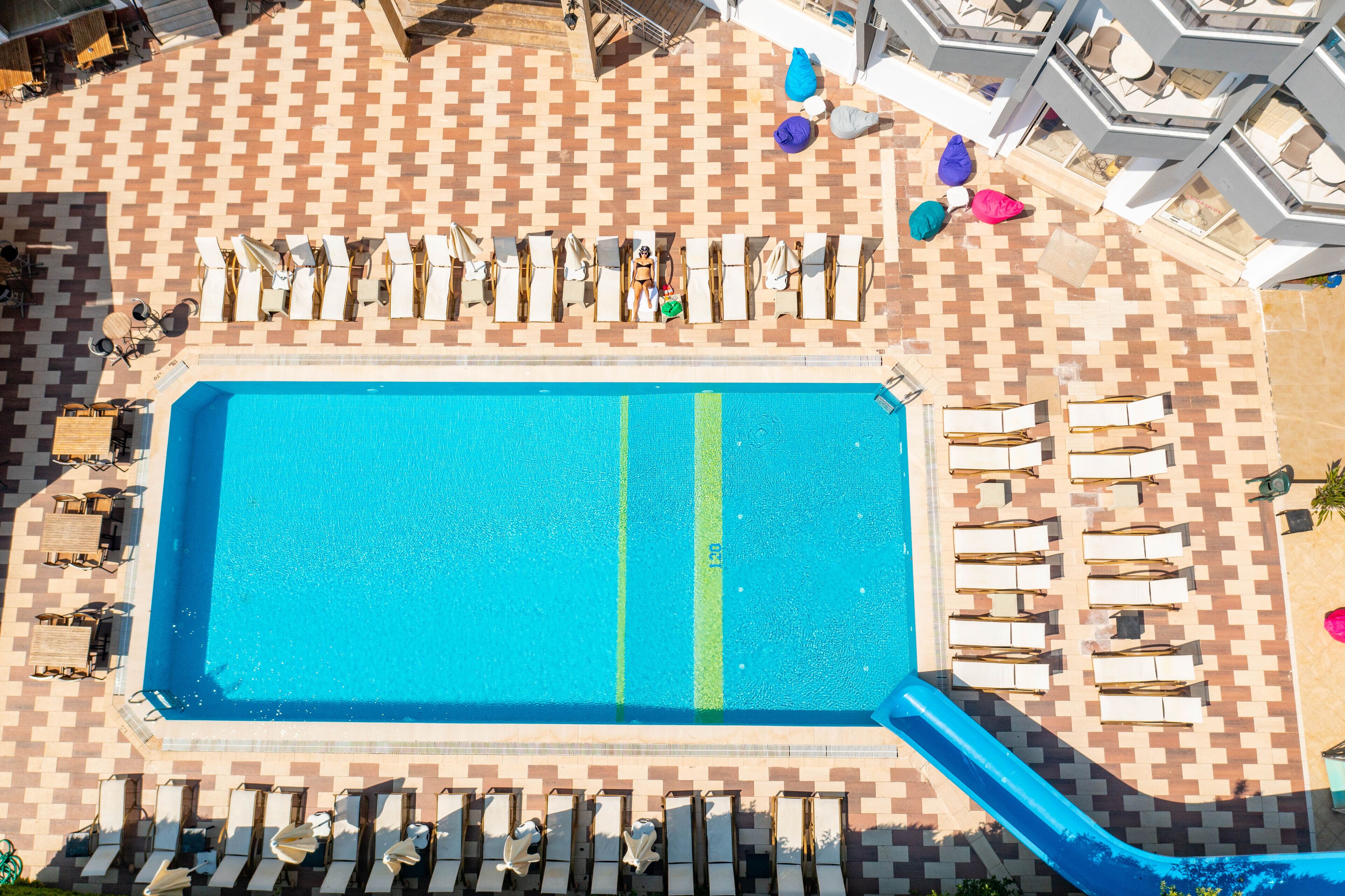 Vue aérienne d’une piscine avec des chaises longues et un toboggan.