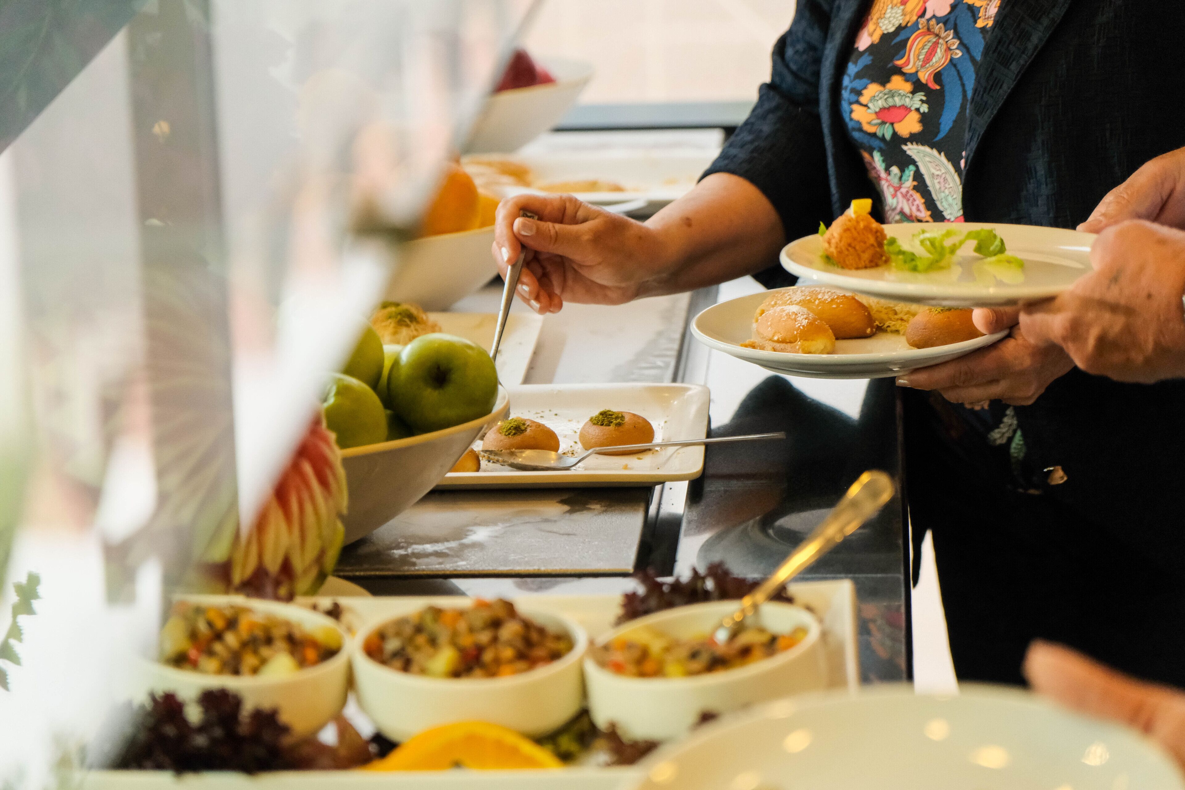 A buffet with various dishes and a person serving food.