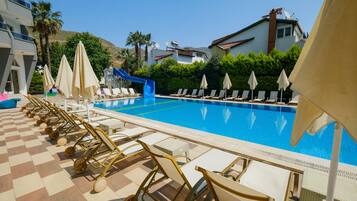A pool area with lounge chairs and umbrellas, a blue slide, and a view of surrounding buildings.