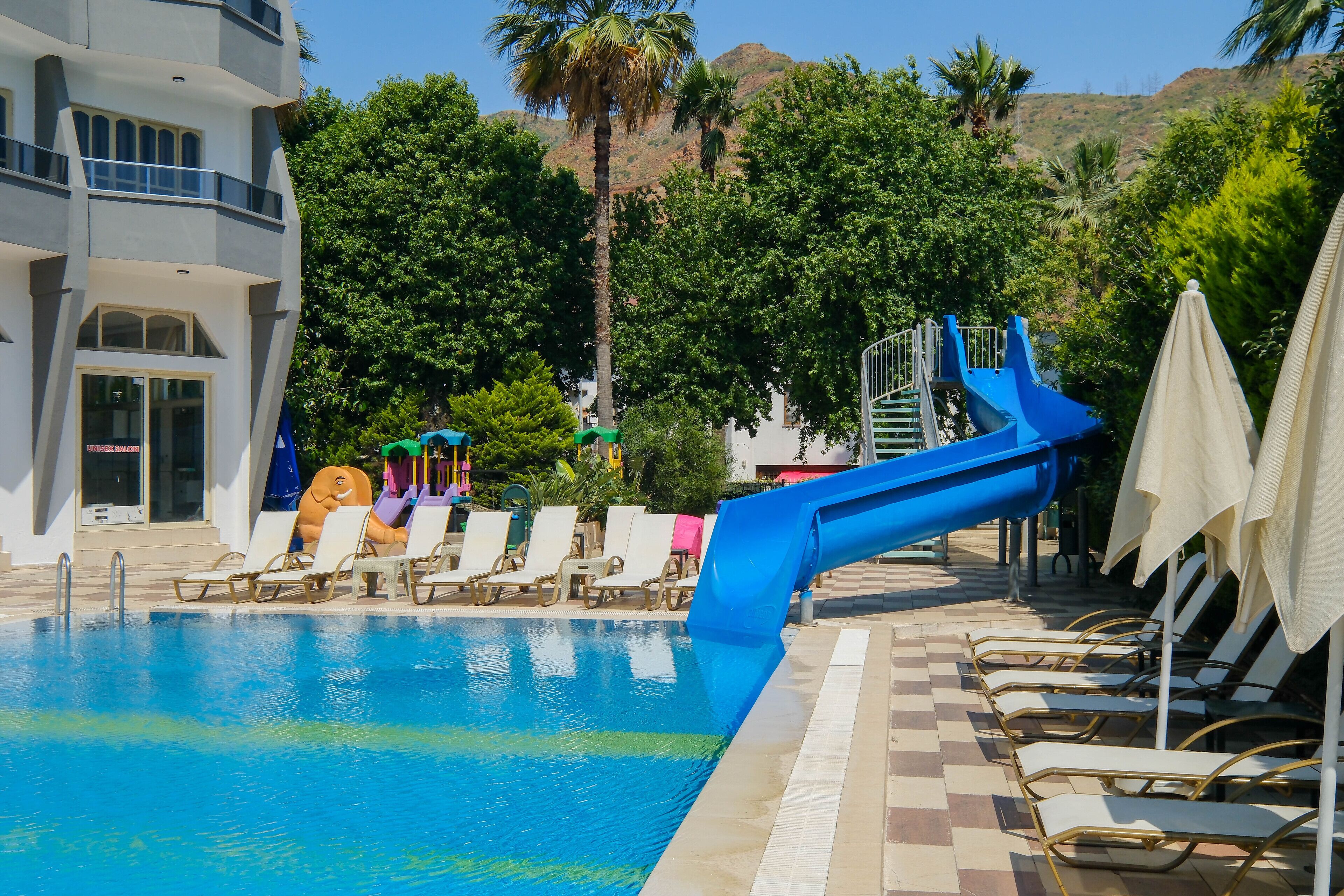A swimming pool with a blue slide, lounge chairs, and a building with a balcony.
