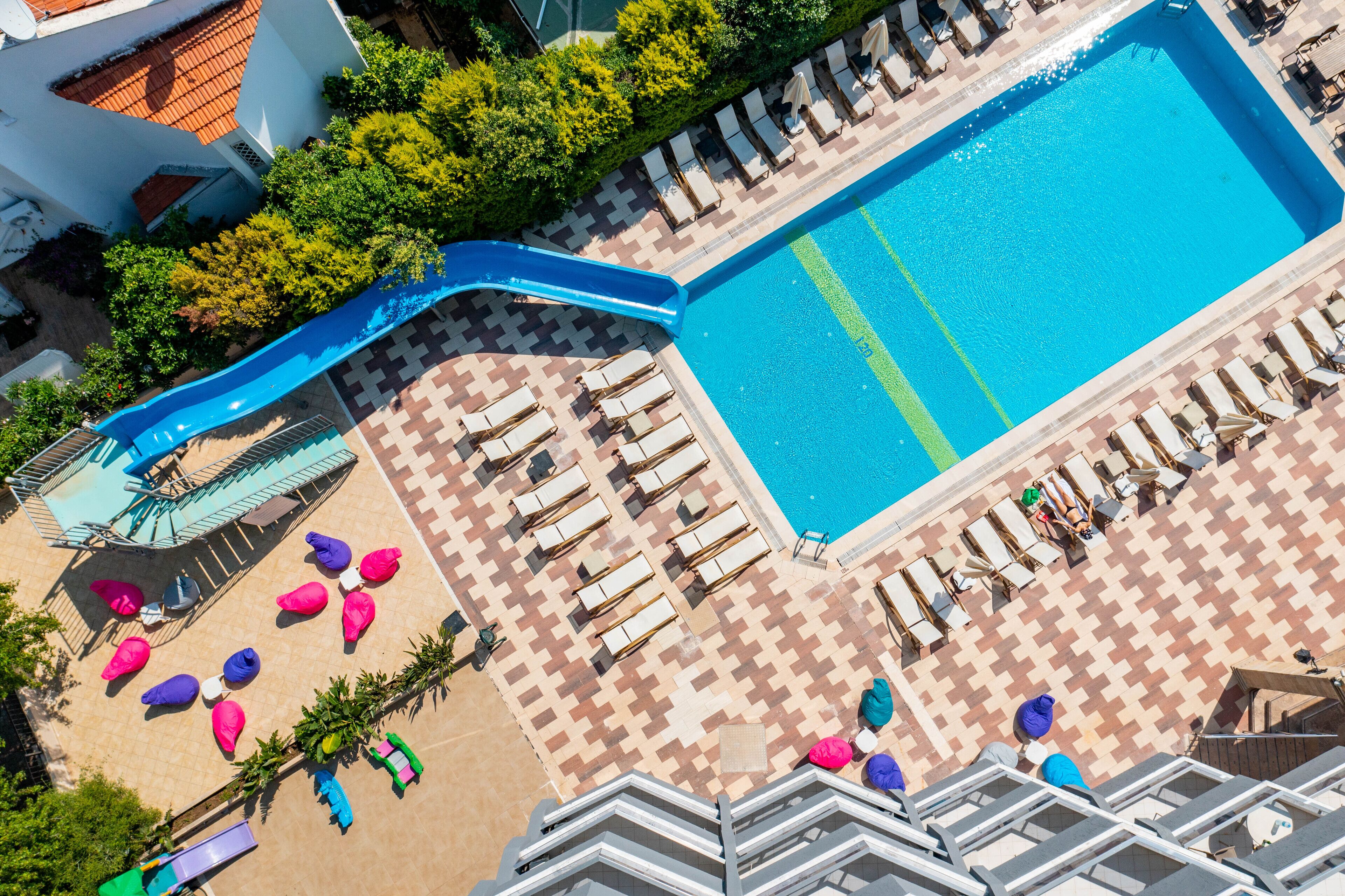 Eine Vogelperspektive auf einen Hotelpoolbereich mit einer blauen Rutsche, Liegestühlen und einem gefliesten Deck.
