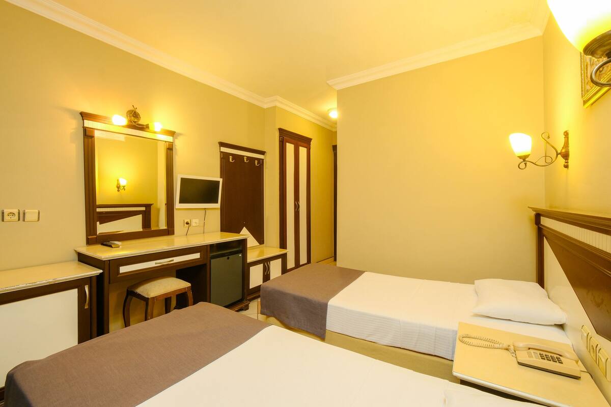 A hotel room with two beds, a desk, a chair, a mirror, and a telephone.