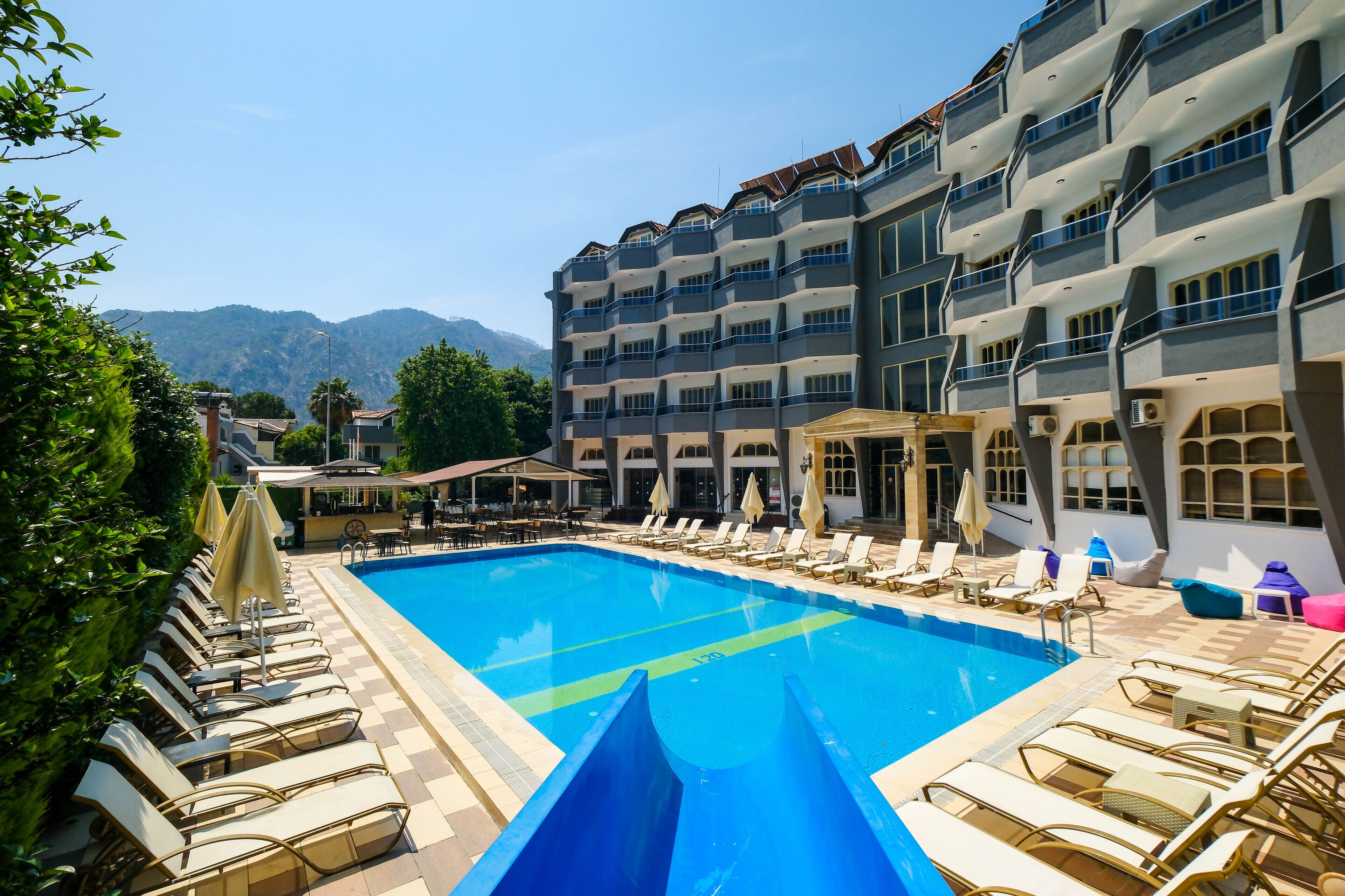 A hotel with a swimming pool, lounge chairs, and a mountain view.