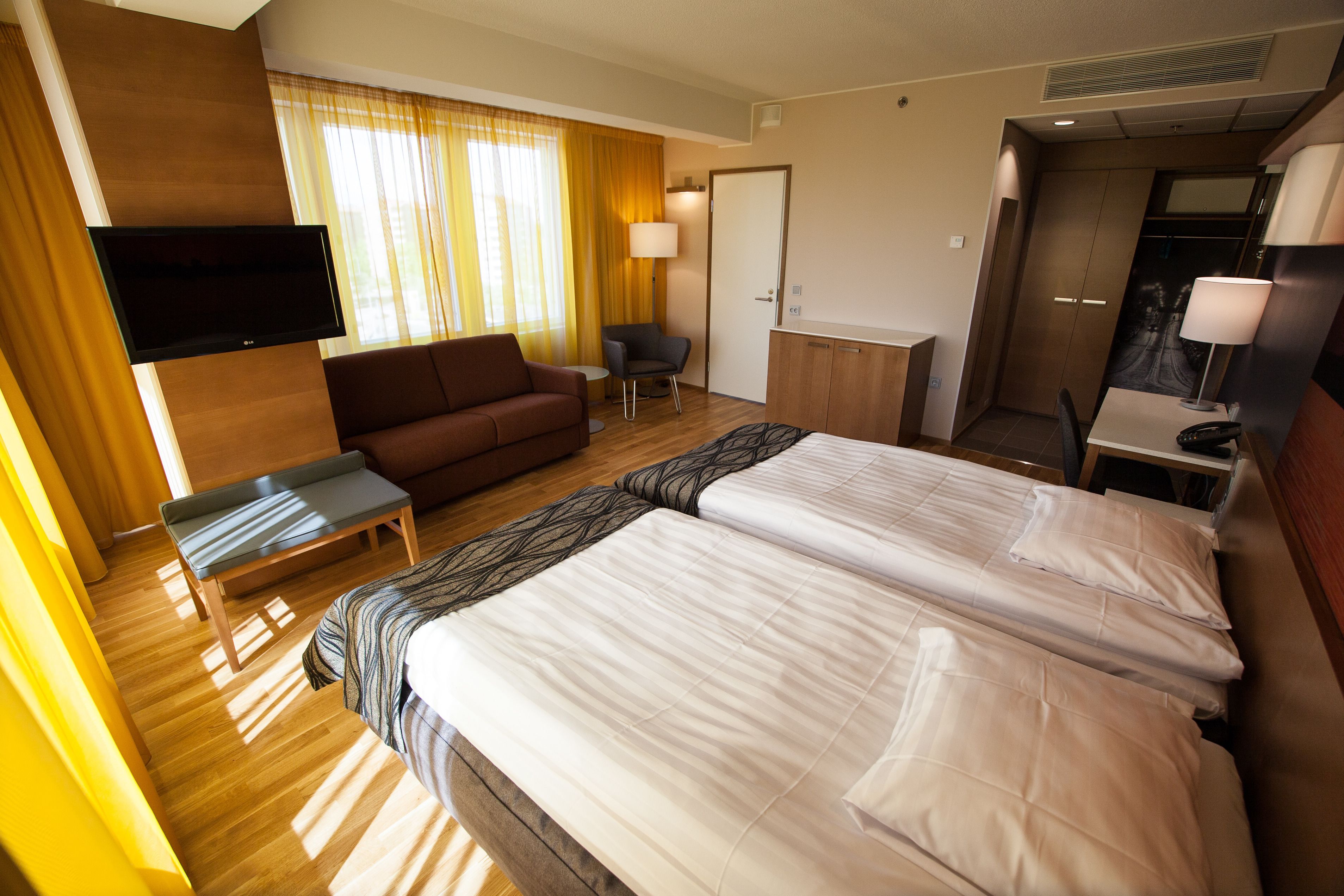 A hotel room with two beds, a sofa, a TV, a desk, and a chair.