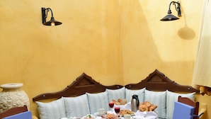 Un coin repas avec une table dressée pour deux personnes, un banc en bois et un mur jaune.