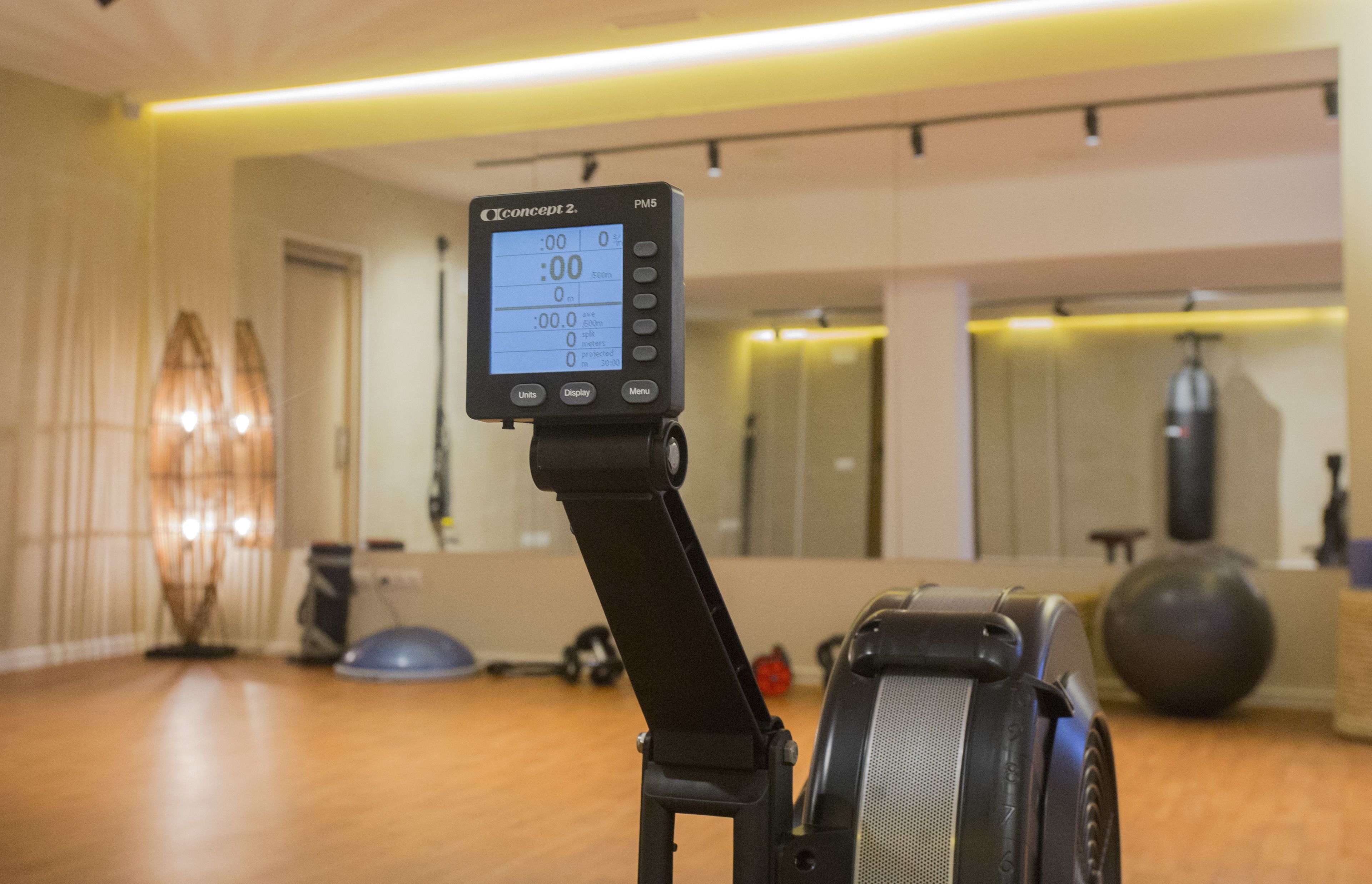 Una bicicleta estática con pantalla digital en una habitación que incluye un espejo, pelotas de ejercicio y una colchoneta de yoga.