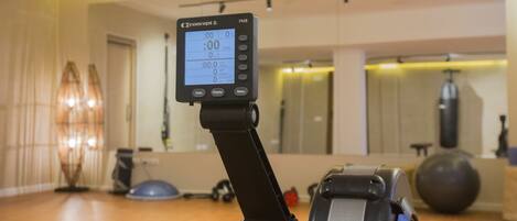 Una bicicleta estática con pantalla digital en una habitación que incluye un espejo, pelotas de ejercicio y una colchoneta de yoga.