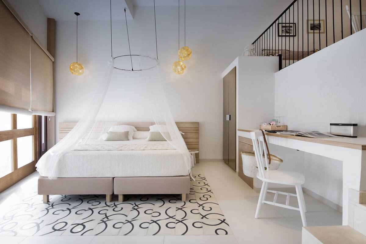 A bedroom with a bed, bedside table, chair, desk, and a staircase.