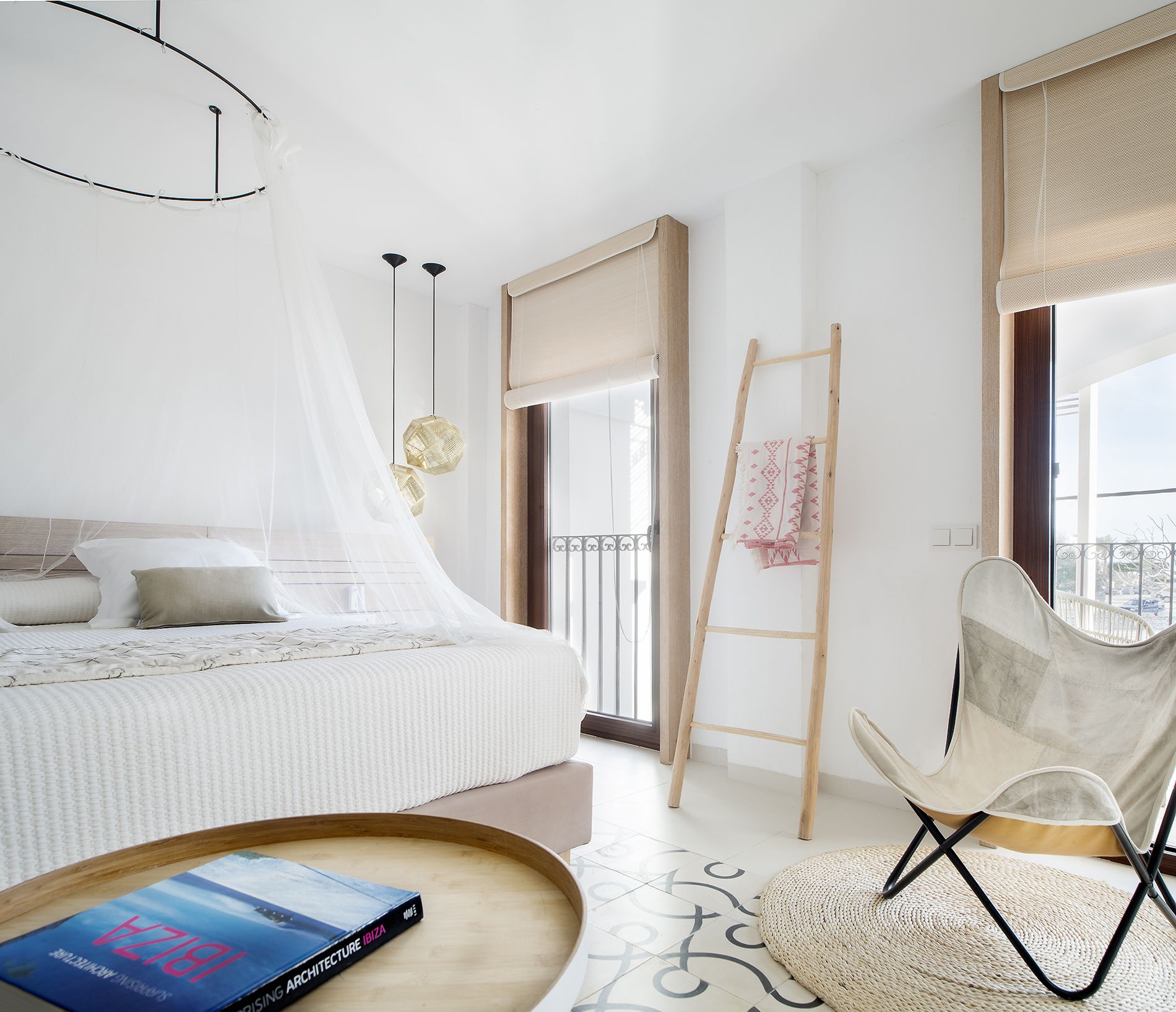 Un dormitorio moderno con una cama, una silla, una escalera y un libro sobre una bandeja.