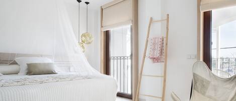 Un dormitorio moderno con una cama, una silla, una escalera y un libro sobre una bandeja.