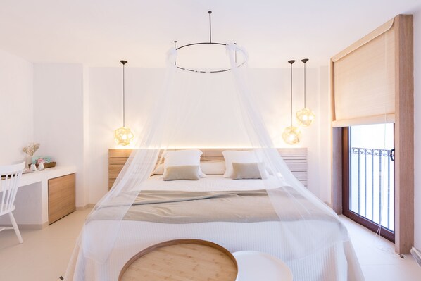 A bedroom with a bed under a canopy, bedside tables with lamps, a desk, and a window with a view.