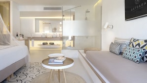 Una camera d'albergo moderna con un letto, un divano, un piccolo tavolino con un libro, uno specchio grande e un angolo doccia.