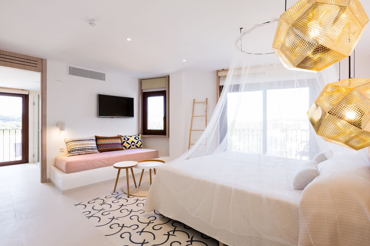 A modern bedroom with a large bed, a seating area with a sofa and a small table, and a large window with a view.