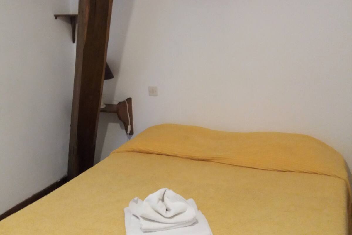 Una habitación con una cama, un cuadro en la pared y una silla de madera.
