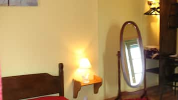 Een slaapkamer met een bed, een nachtkastje met een lamp, een spiegel en een rood tapijt.