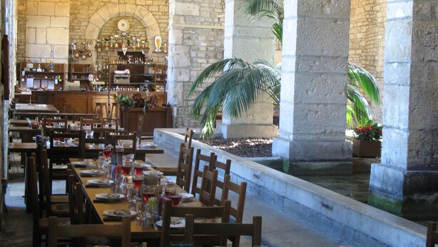 Un restaurante con paredes de piedra, mesas y sillas de madera. Hay plantas y una fuente en el centro.