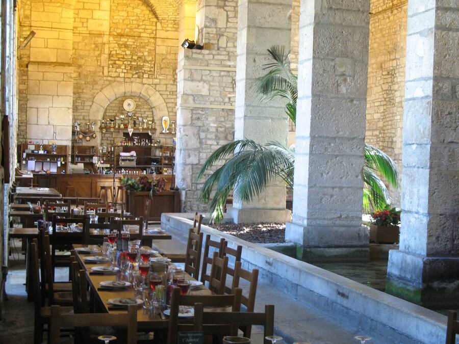 Un restaurante con paredes de piedra, mesas y sillas de madera. Hay plantas y una fuente en el centro.