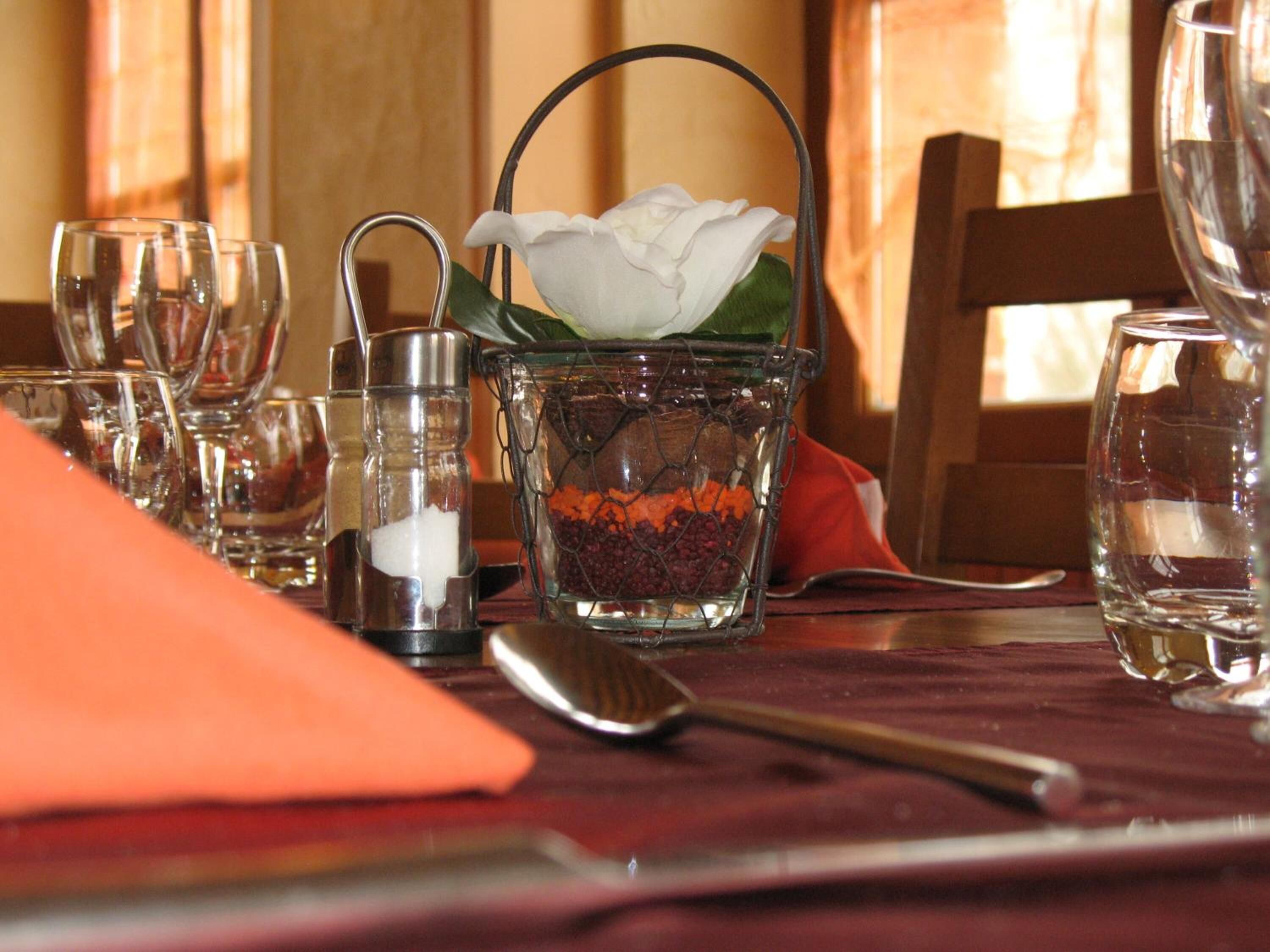 A dining table with a clear glass container holding a white flower, salt and pepper shakers, and a metal spoon.