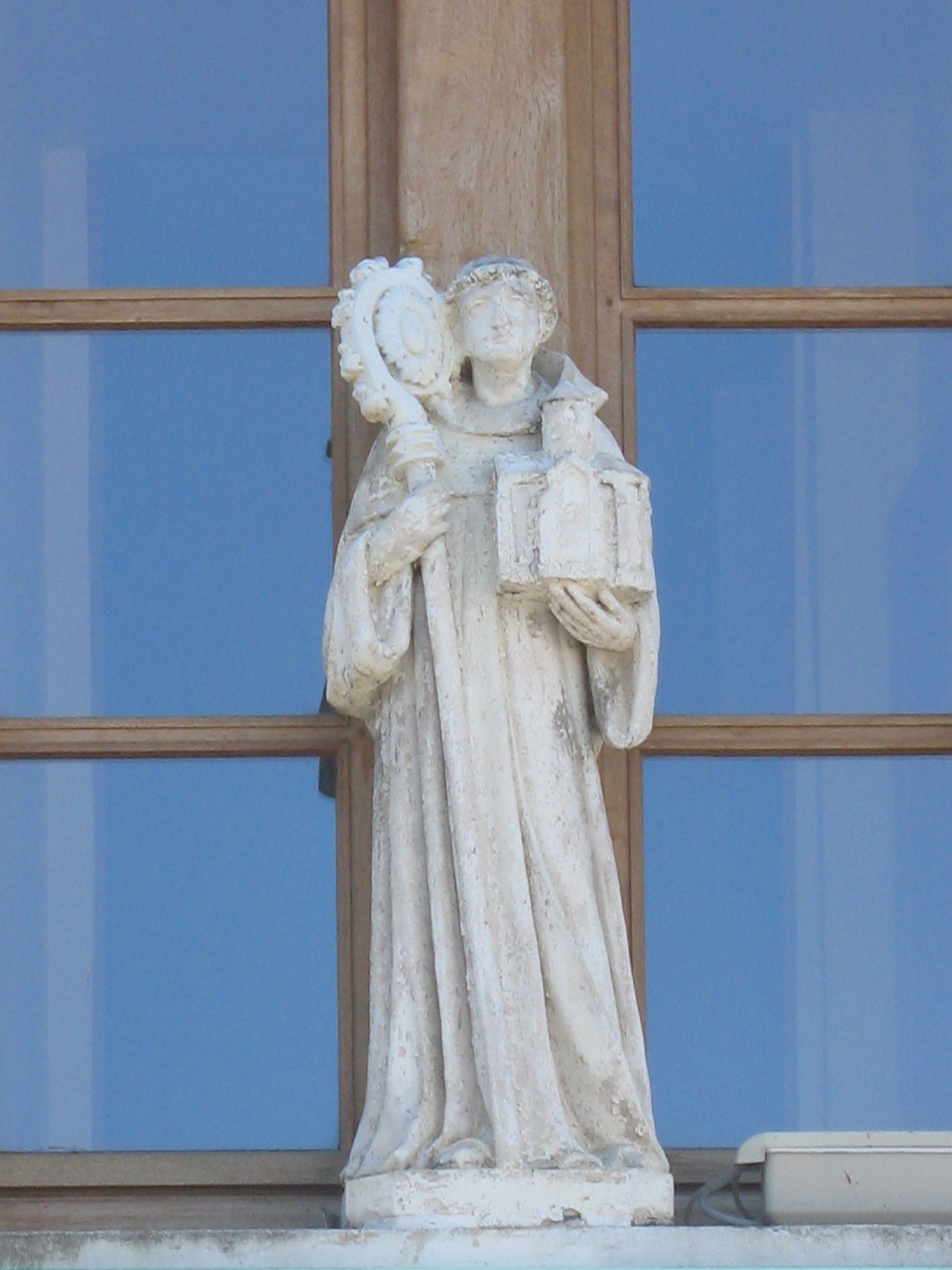 Una estatua de piedra de una figura sosteniendo un libro y un rollo, sobre un fondo azul con paneles de madera.